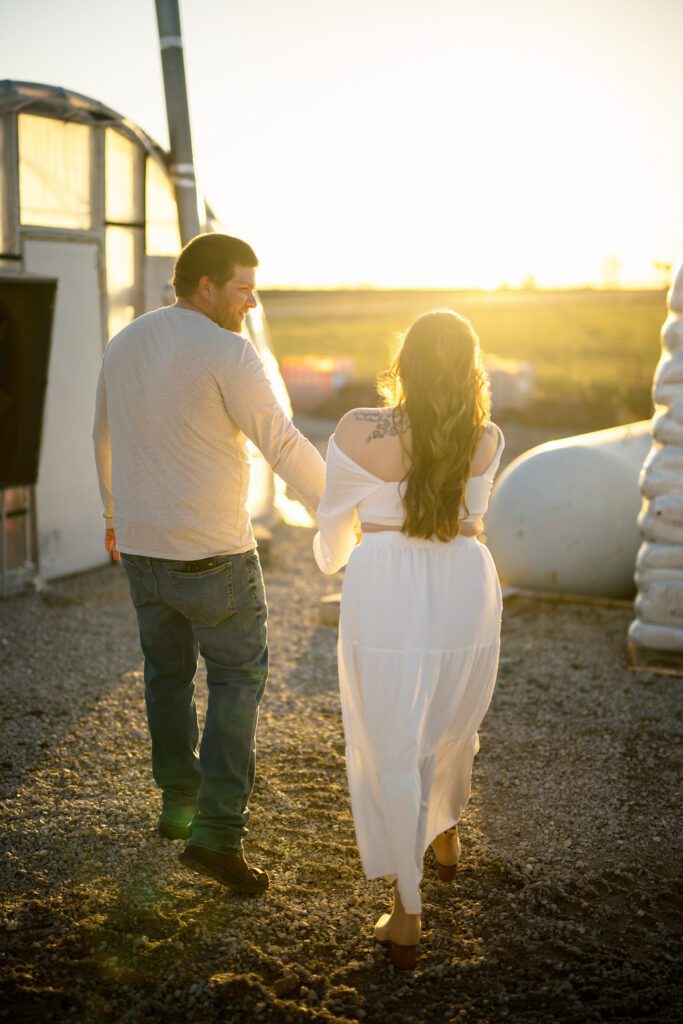 engaged couple wearing white walking into golden sunlight at greenhouses