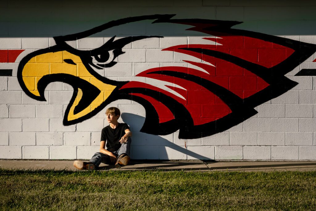 Southern boone county high school senior sitting in front of red and yellow eagle painting on wall with bright sunshine