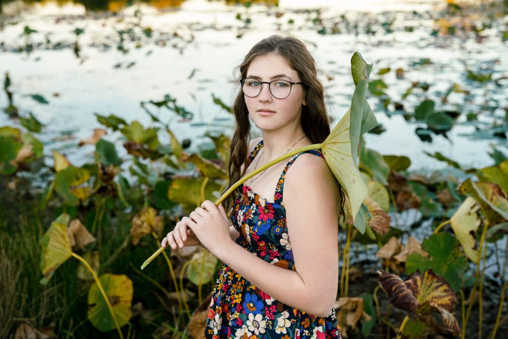 Battle Senior High School Girl wearing floral dress holds a lillypad over her shoulder by lake